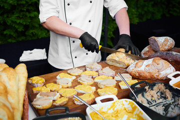 Mid-section of waiter chopping bread roll on chopping board on outdoor event