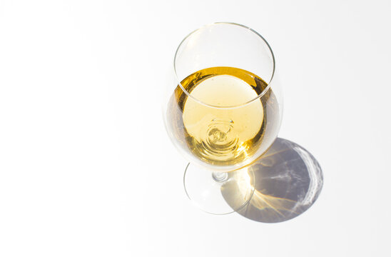 Top view of glass with white fresh wine on white background with sparkling shadows. Free copy space.  Concept of summer drinks.