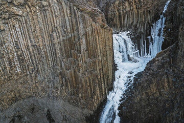Litlanesfoss waterfall frozen with basalt columns from aerial view