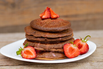 chocolate pancakes with strawberries on a white plate.