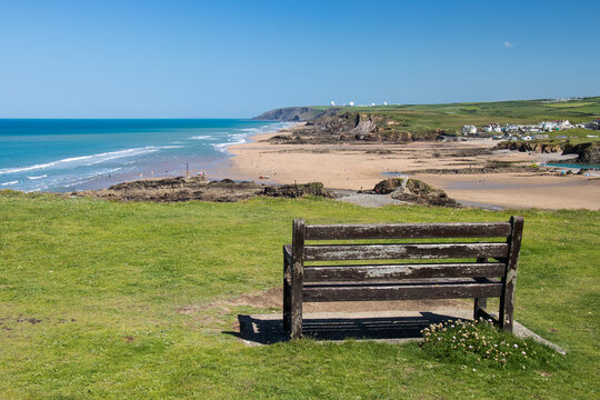 Wooden bench on Cornish cliff overlooking crooklets beach in Bude, Cornwall on a sunny day with a blue sky.
