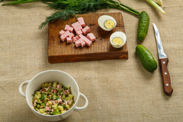 Okroshka in a clay plate on the table on a tablecloth next to an egg sausage and cucumbers on...