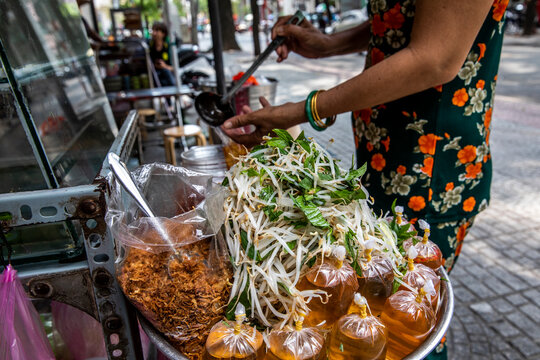A Street Food Cook Adds Final Condiments To An Entree On Saigon Street