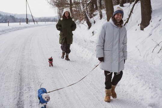 women laugh walking dogs in snow jackets in frozen winter country road