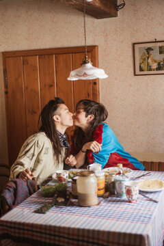 Queer female couple smile and kiss over birthday breakfast in Czechnia