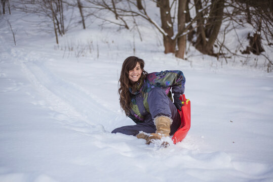 happy woman in snow suit smiles riding down hill on toboggan