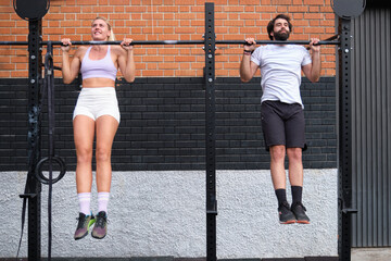 Young man and woman doing pull ups at a crossfit pull up bar