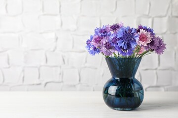 Bouquet of beautiful cornflowers in glass vase on white wooden table. Space for text - obrazy, fototapety, plakaty