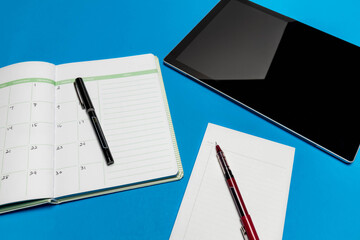 Planner schedule calendar and to do list reminder agenda next to computer tablet work from home concept with July 4th written down in book isolated on blue background