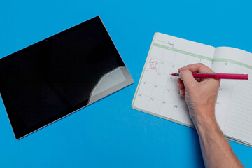 Planner schedule calendar and to do list reminder agenda next to computer tablet work from home concept with July 4th written down in book isolated on blue background