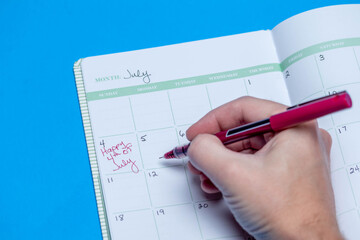 Planner schedule calendar and to do list reminder agenda work from home concept with happy July 4th handwritten down in book isolated on blue background
