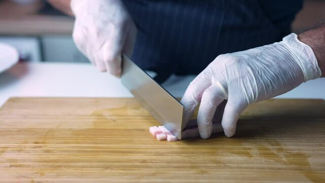 Closeup of male cook or chef cuts the bacon guanciale into thin strips on a wooden cutting board in a restaurant or at home.