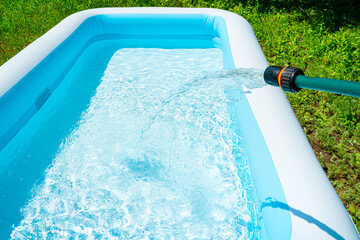 Filling the inflatable pool with water. Swimming pool in the summer garden. - obrazy, fototapety, plakaty
