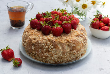 Homemade gingerbread cake garnished with fresh strawberries on a light gray table. Summer still life outdoors.