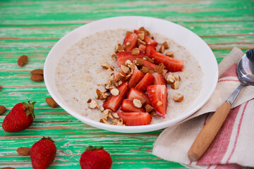 Oatmeal porridge with strawberries and almonds in a white plate on a rustic background