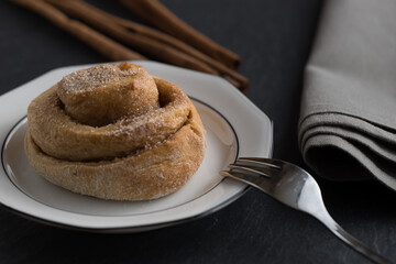 cinnamon roll on a black slate background, dark and moody, in background cinnamon sticks, selective focus on cinnamon bun