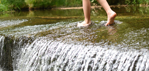 Kids legs walkingin watere  in stream in the summer. Outdoor, barefoot, holiday concept