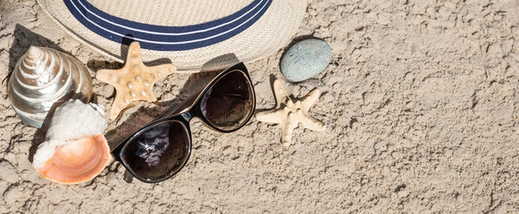 The concept of a holiday at the sea. Shells, a straw hat, sunglasses on the sand. Background for summer holidays with space for text. Top view.