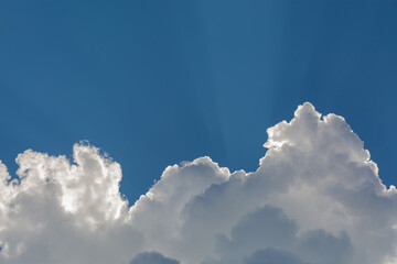 White fluffy clouds on the background of blue sky. The illumination of the Sun emphasizes their...