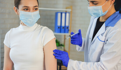 Caucasian doctor is vaccinating the patient wearing medical mask at the office