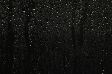 Glass with rain drops on black background