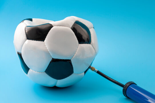 Team sports and competitive athletics concept with deflated football or soccer ball being inflated with a manual pump isolated on blue background