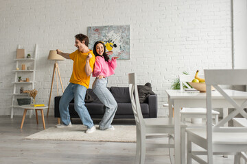 smiling young couple in casual clothes dancing in modern living room