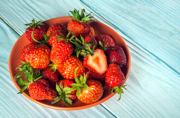 The full plate of strawberries and a cut piece on a blue table. Strawberry Diet Idea