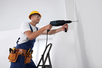Worker using electric drill indoors, low angle view