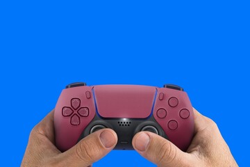 Fototapeta premium Male hand holding a Next Generation red game controller isolated on blue background.
