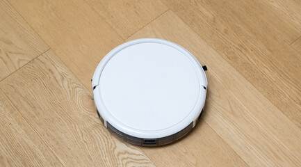 Cleaning robot vacuum in action on the hardwood parquet, home and domestic life. RF photo, no logos
