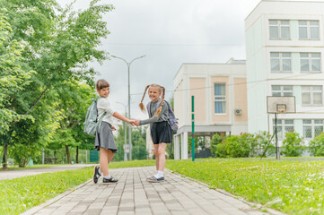 Fototapeta na wymiar two cute happy girls schoolgirls with backpacks are playing near the school. High quality photo