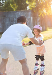 Father teaching the daughter skating on rollers.