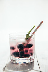 Summer cocktails and fresh drinks concept with various fresh berries. A glass with water, a sprig of rosemary and blueberries on the table. Vertical photo. Copy space