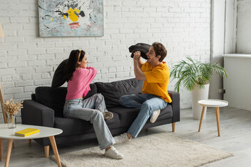 Fototapeta premium smiling young couple fighting with pillows on couch in living room