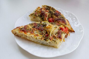 Pieces of homemade cheese focaccia with tomatoes, on a white porcelain plate
