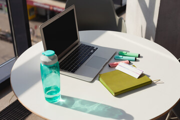 A laptop on the desktop in a bright office, clear water in a bottle, a diary