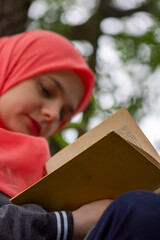 Muslim female student reading a book in nature, outdoor