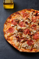 Pizza with sun-dried tomatoes, spicy sausage, chicken, onions, honey mushrooms, mozzarella cheese, spices and tomato sauce. On a dark background.