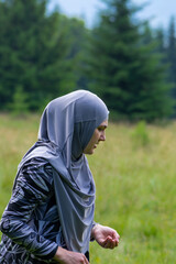Muslim girl wearing grey hijab walking on the meadow