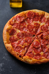 A closeup of a pepperoni pizza. Pizza with spicy sausage, tomato sauce and mozzarella cheese. Flat lay. On a dark background.