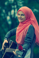 Portreit of happy muslim girl wearing hijab trying to play guitar outdoor