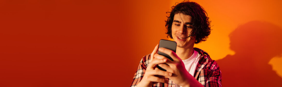 Cheerful Curly Man Using Mobile Phone On Orange Background, Banner