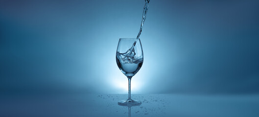 banner with pouring water into a transparent glass for wine. light blue background with water splashes and copy space