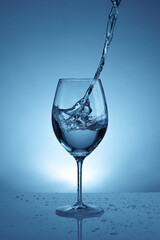 pouring water into a transparent glass for wine. light blue background with water splashes