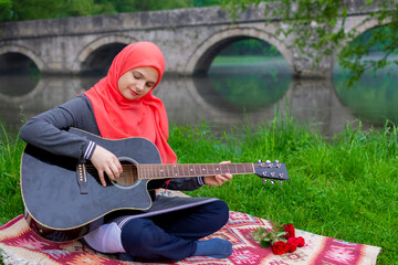 Preaty young muslim girl traying to play acoustic guitar on the river bank during haze