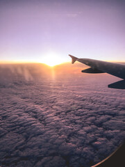 Fototapeta na wymiar Plane wing flying over the clouds and colorful sunset in the horizon