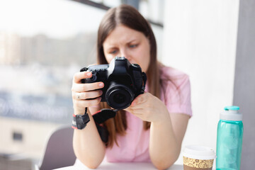 a photographer girl in a pink blouse examines the work done on the camera screen front view