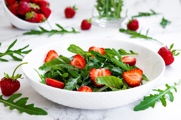 Summer salad of strawberry with arugula, spinach leaves in white plate on marble table with salad leaves and fresh strawberry fruits around. Strawberry salad recipe DIY. Step 2.