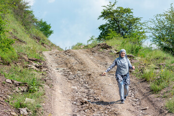Young muslim girl wearing sport clothes walking alone on the rural mountain road. Woman with hijab in the nature. Islam religion concept